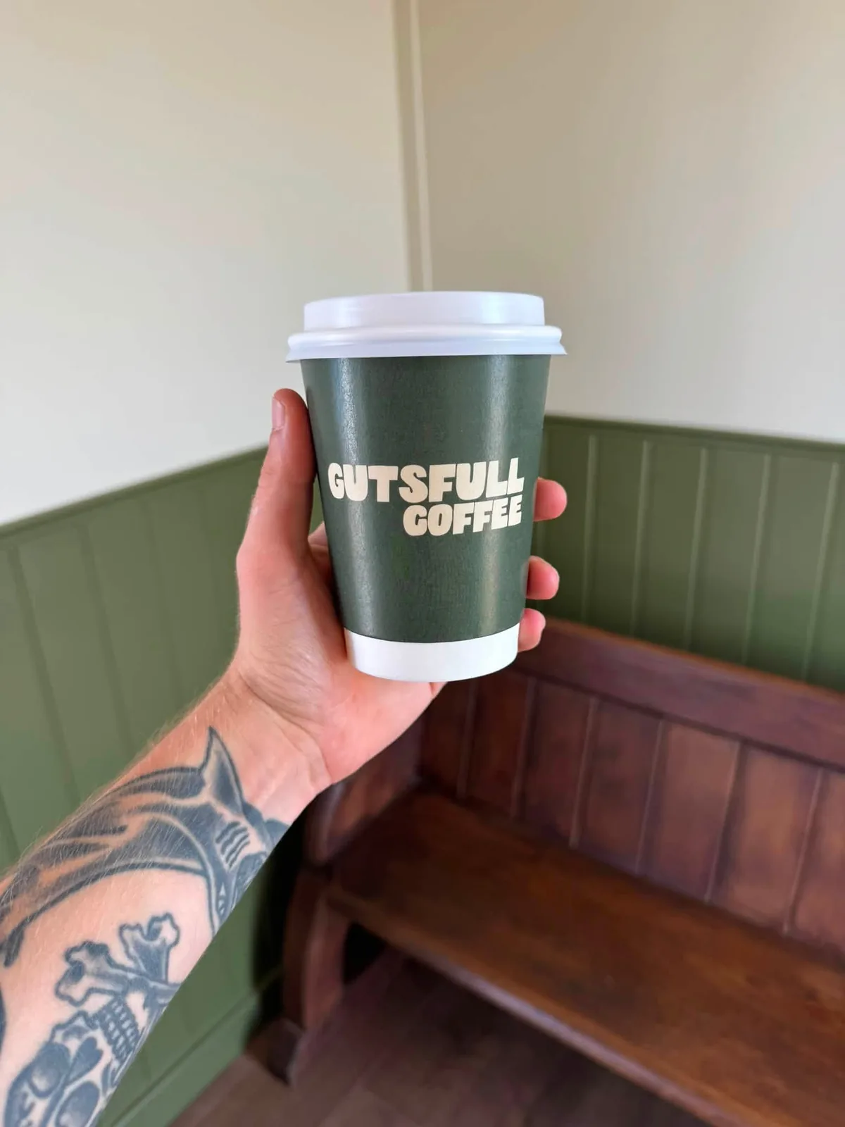 A Gutsfull cup held up against the olive panelling inside the shop