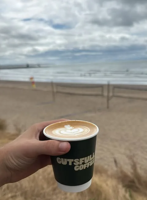 A Gutsfull flat white held up on the sand at Coney Beach, Porthcawl