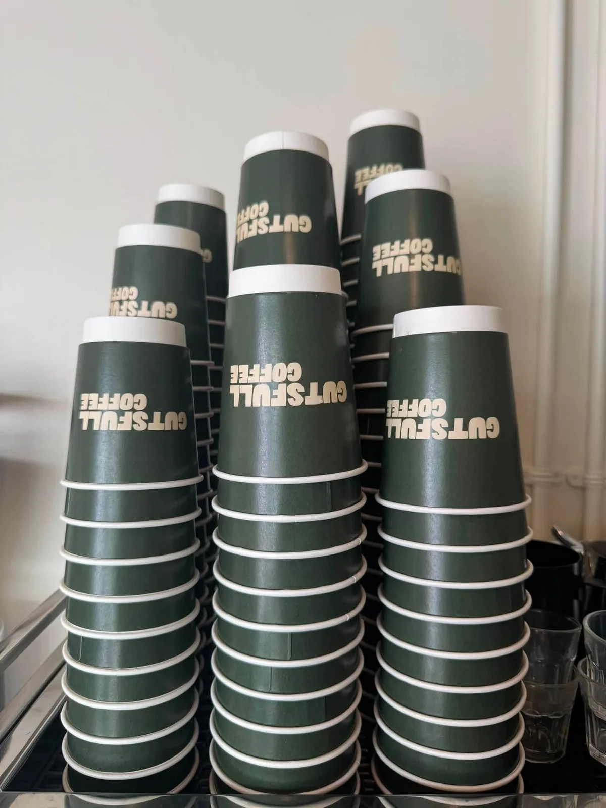 Stacks of olive Gutsfull cups waiting on top of the espresso machine